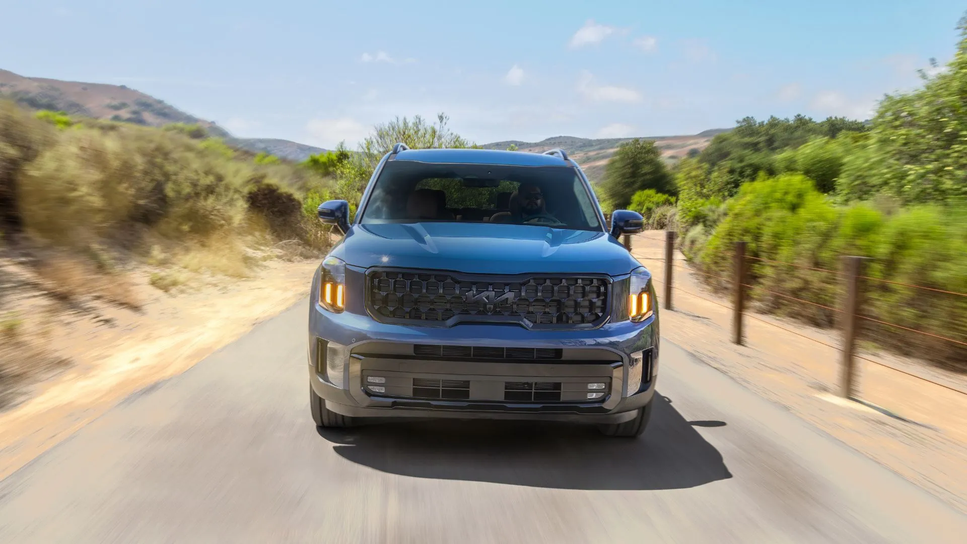 Phần đầu xe Kia Telluride 2025 màu xanh dương đang di chuyển trên con đường nông thôn, phản ánh sự mạnh mẽ và linh hoạt của mẫu SUV này.