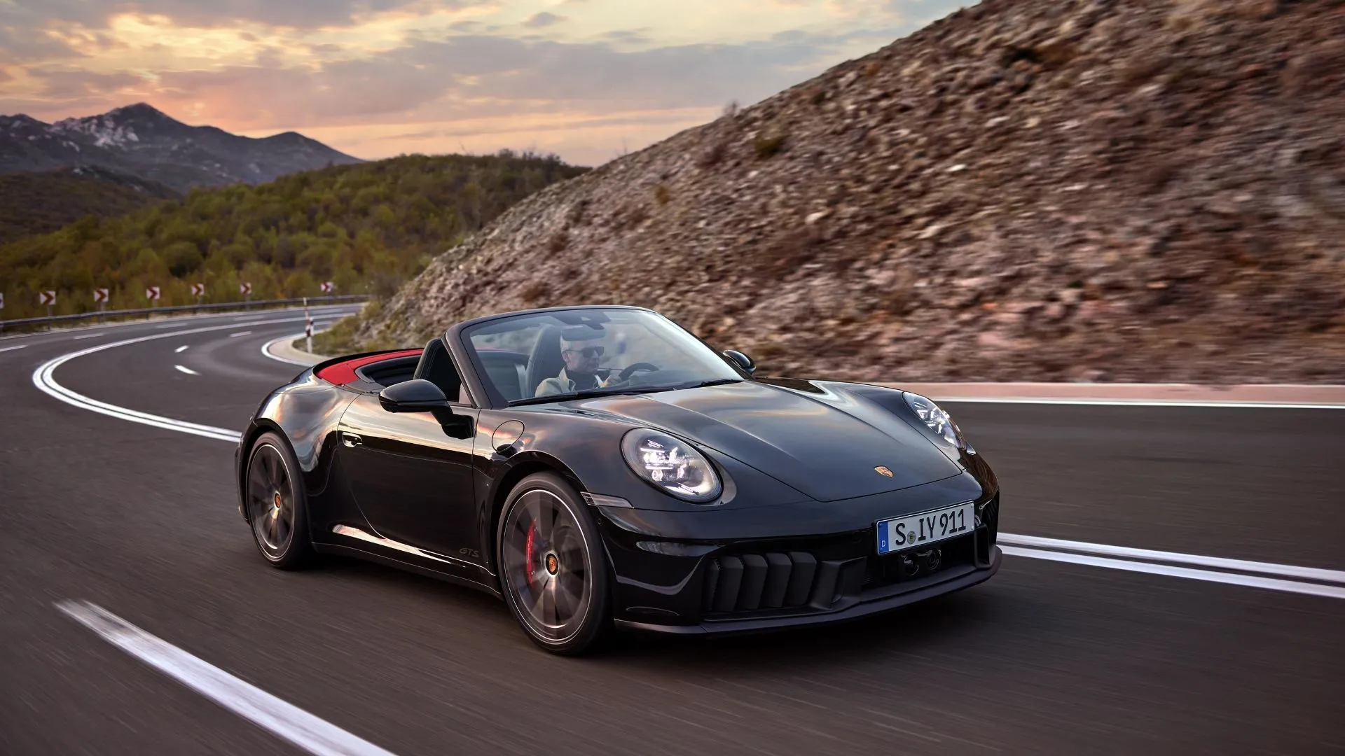Porsche 911 Carrera GTS Cabriolet Hybrid 2024 màu đen chạy trên đường núi quanh co, kết hợp hiệu suất thể thao và công nghệ hybrid