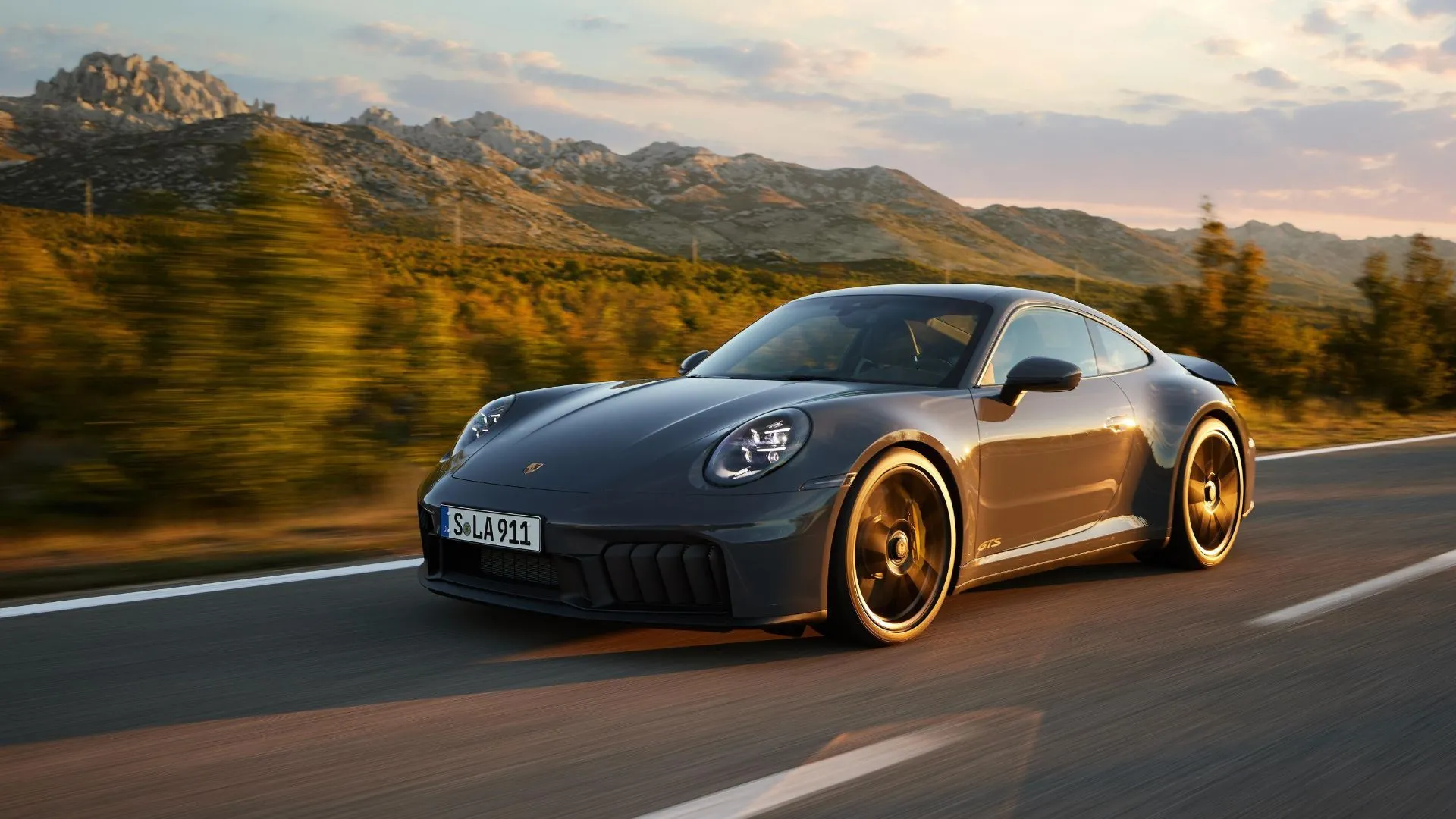Porsche 911 Carrera GTS Hybrid 2024 màu xám di chuyển trên con đường núi uốn lượn