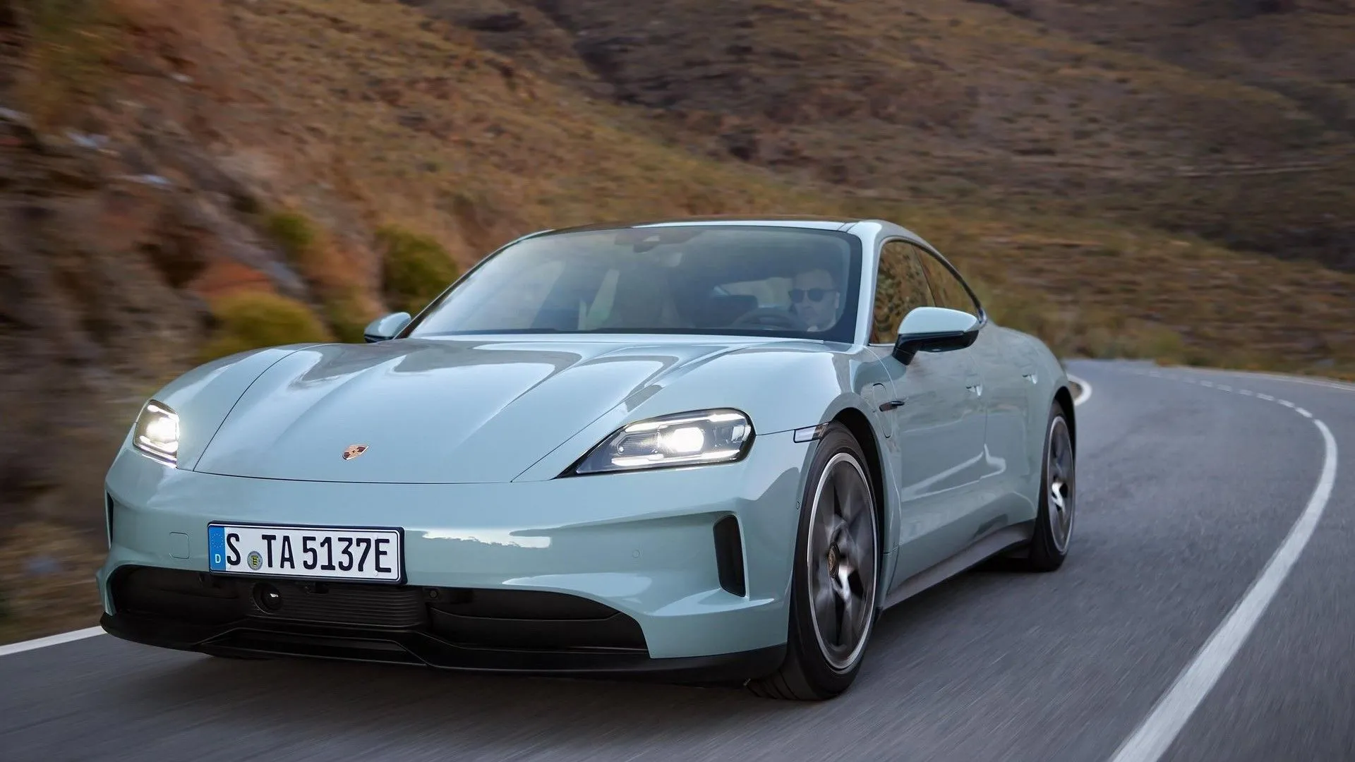 Porsche Taycan 2025 màu xanh dương sẫm đang di chuyển trên đường, mẫu sedan điện hiệu suất cao kết hợp công nghệ tương lai và khả năng vận hành đặc trưng của Porsche