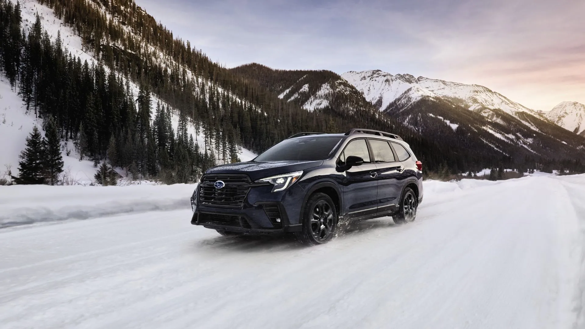 Subaru Ascent 2025 màu xanh đậm đang lái trong tuyết với núi non phía sau, góc nhìn ba phần tư phía trước.