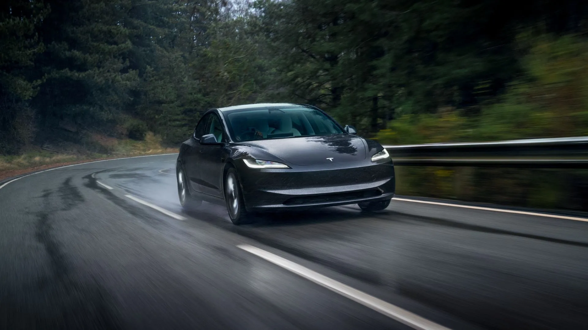 Tesla Model 3 2025 màu xám di chuyển trên đường ướt, thể hiện công nghệ xe điện tiên tiến và thiết kế tối giản.