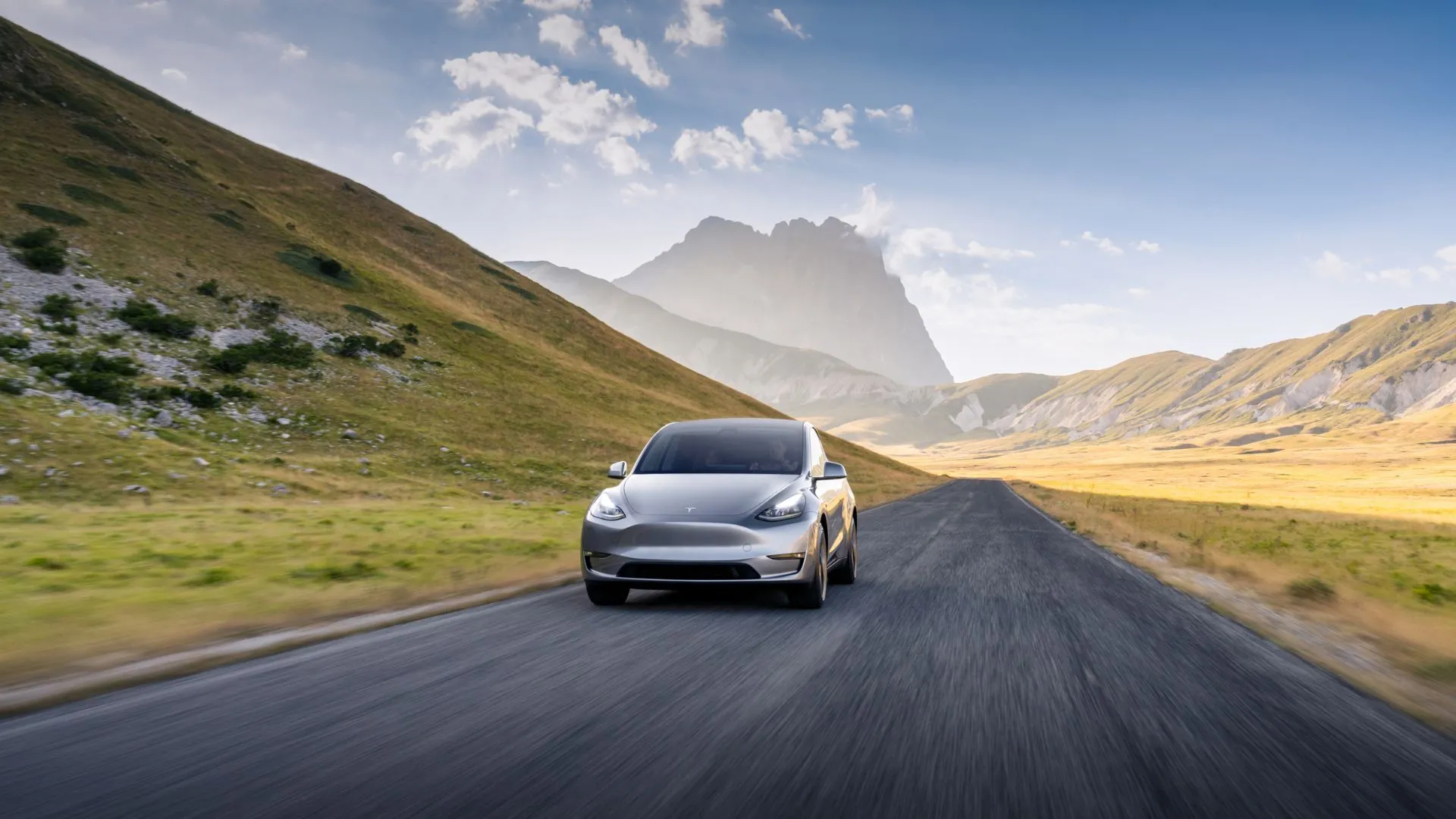 Tesla Model Y màu bạc chạy trên đường nông thôn, phía sau là núi non hùng vĩ, thể hiện sự linh hoạt