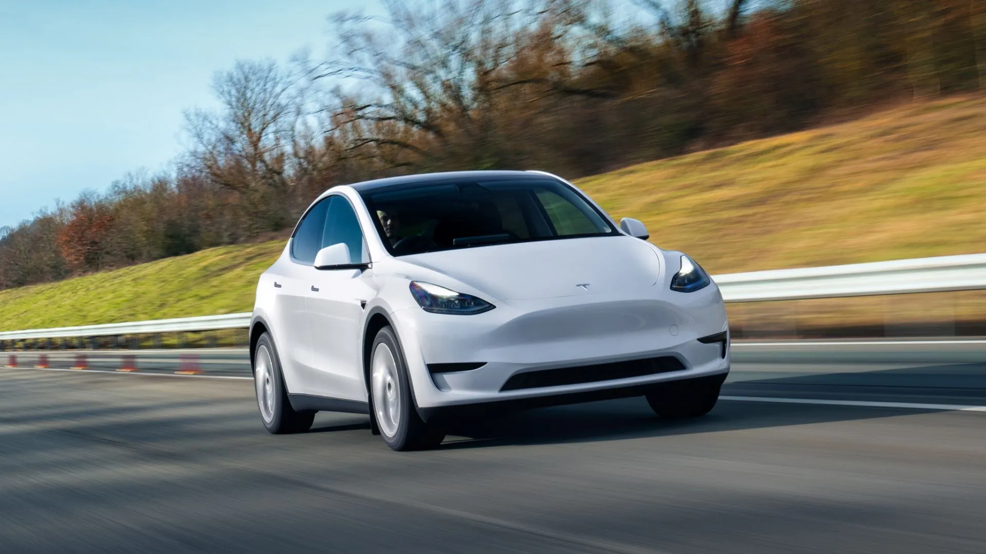 Tesla Model Y màu trắng đang di chuyển trên đường cao tốc, nhìn từ góc trước-bên, thể hiện thiết kế hiện đại và sự năng động