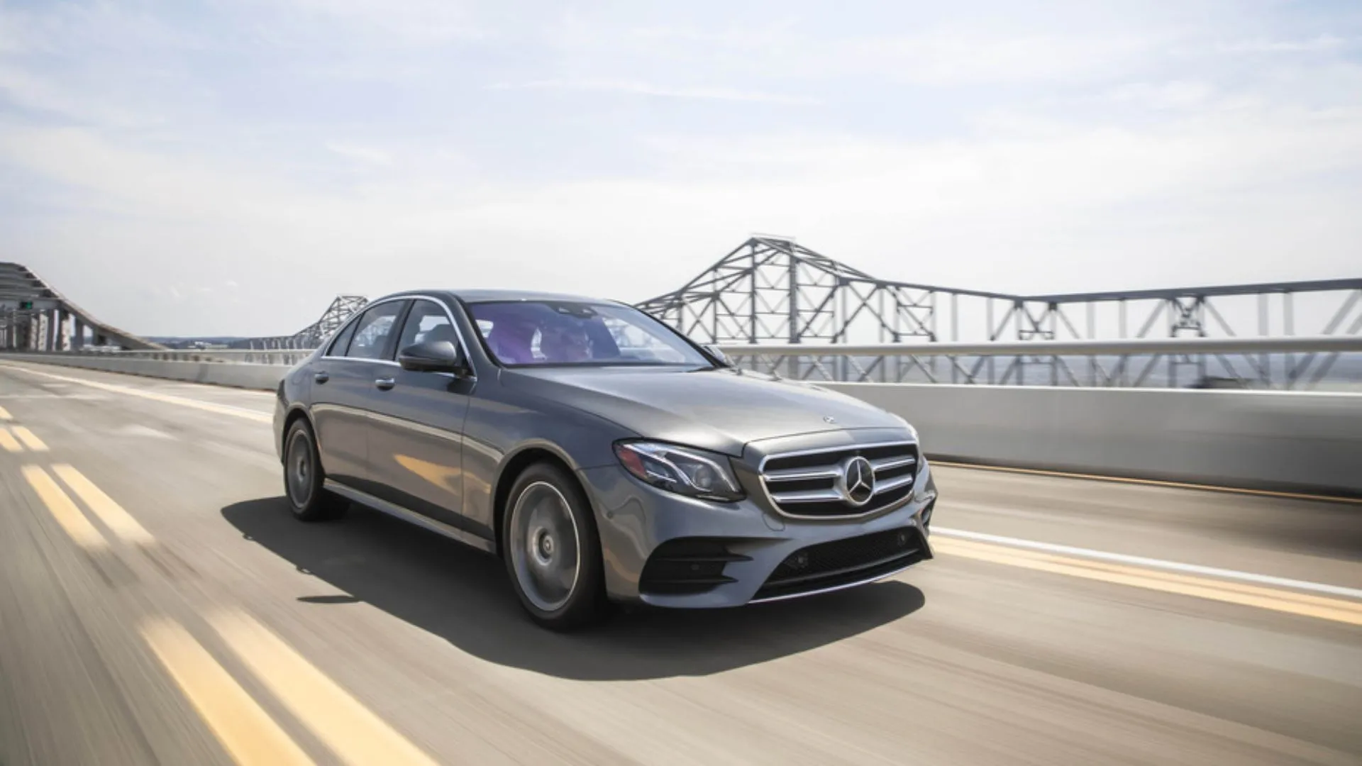 Thiết kế động, góc 3/4 phía trước của chiếc Mercedes-Benz E-Class 2019 màu xám đang lái qua cầu.