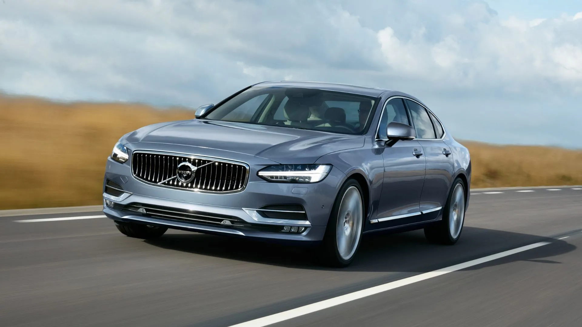 Thiết kế động, góc 3/4 phía trước của chiếc Volvo S90 2019 màu xanh đang lái trên một con đường nông thôn.