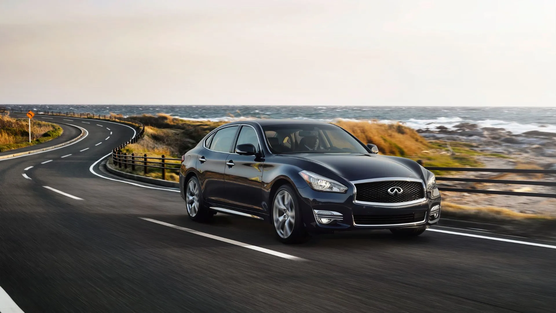 Thiết kế góc 3/4 phía trước của chiếc Infiniti Q70L 2015 đang lái trên con đường quanh co bên bờ biển.