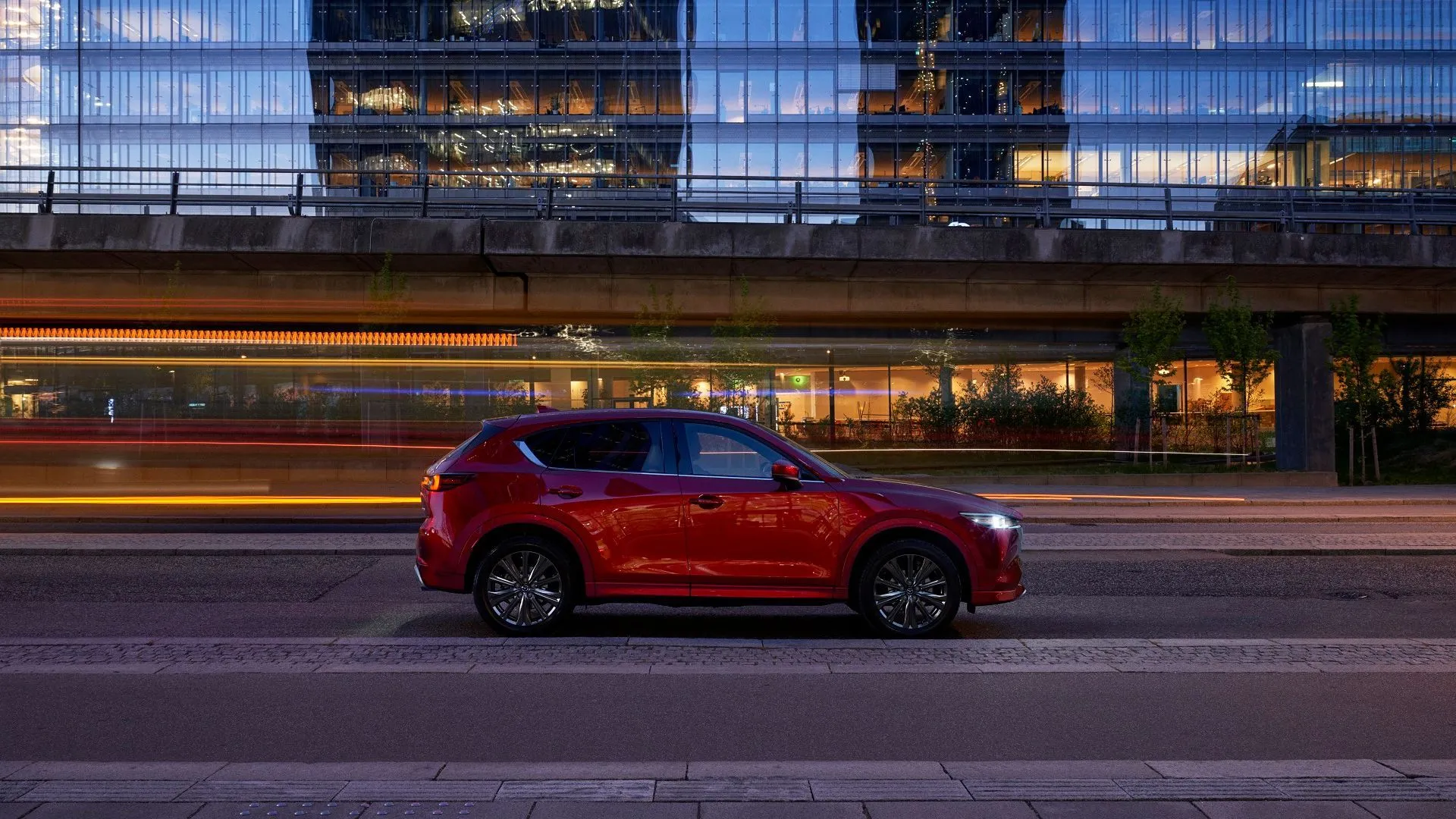 Toàn cảnh bên hông của mẫu Mazda CX-5 màu đỏ đang lướt đi trên phố đêm