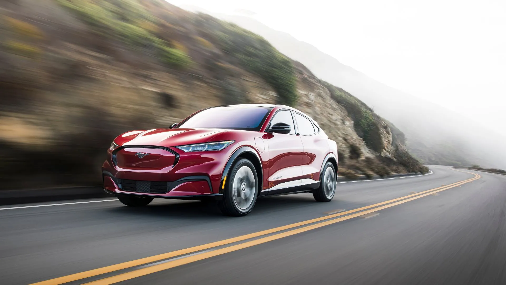 Toàn cảnh chiếc Mustang Mach-E 2021 màu đỏ đang lái trên con đường nông thôn quanh co.