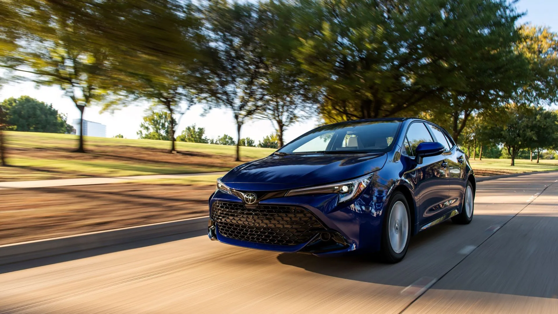 Toyota Corolla Hatchback SE 2025 màu xanh dương chạy trên con đường rợp bóng cây