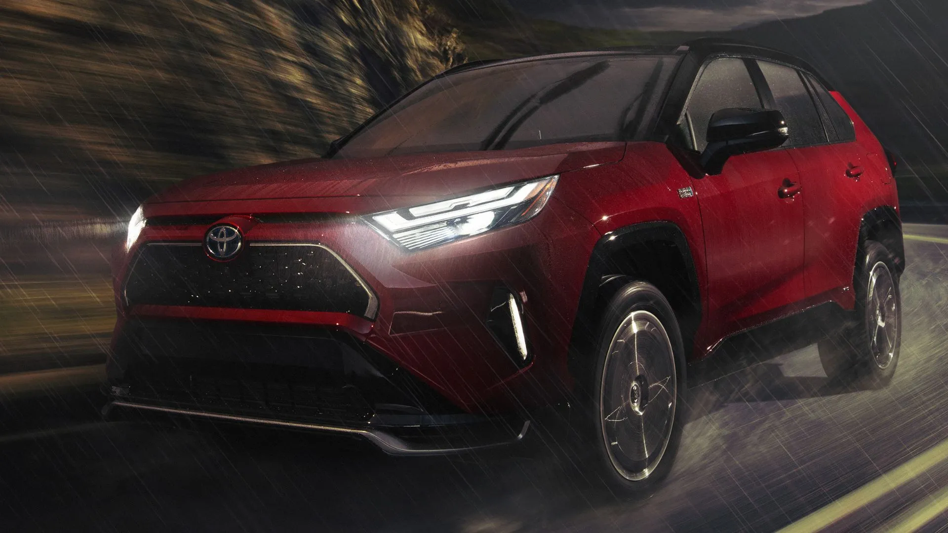 Toyota RAV4 Prime XSE 2024 màu đỏ di chuyển trên đường quê trong mưa, minh họa khả năng vận hành ổn định của mẫu xe PHEV này.