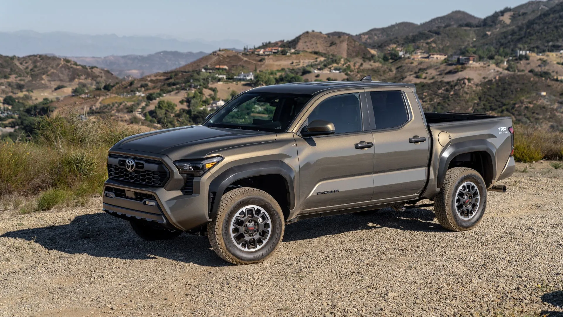 Toyota Tacoma TRD 2025 màu đồng đậu trên sỏi với núi non phía sau, góc nhìn ba phần tư phía trước.