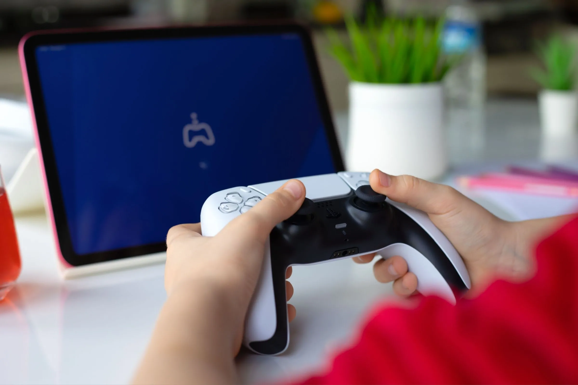 Trẻ em cầm tay cầm DualSense PS5 và iPad Air, tượng trưng cho khả năng chơi game PS5 linh hoạt trên nhiều thiết bị với Remote Play.