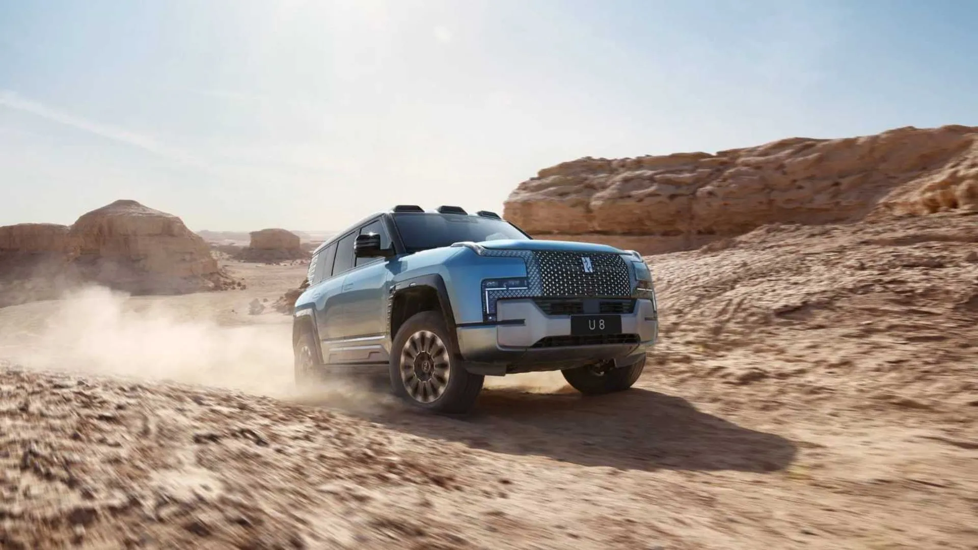 Xe SUV điện Yangwang U8 màu bạc đang vượt địa hình trên sa mạc, chứng tỏ khả năng off-road mạnh mẽ và thiết kế hầm hố.