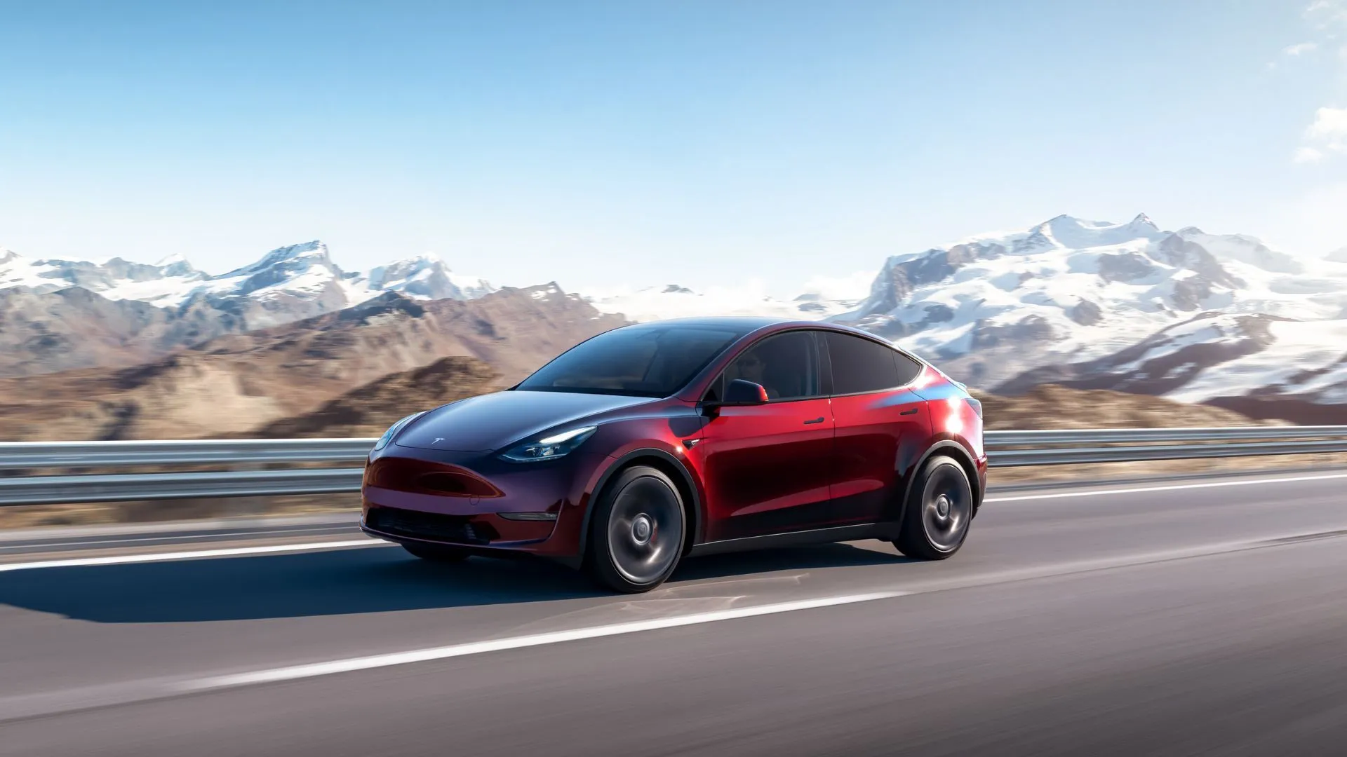 Xe Tesla Model Y màu đỏ trên đường nông thôn với núi phủ tuyết