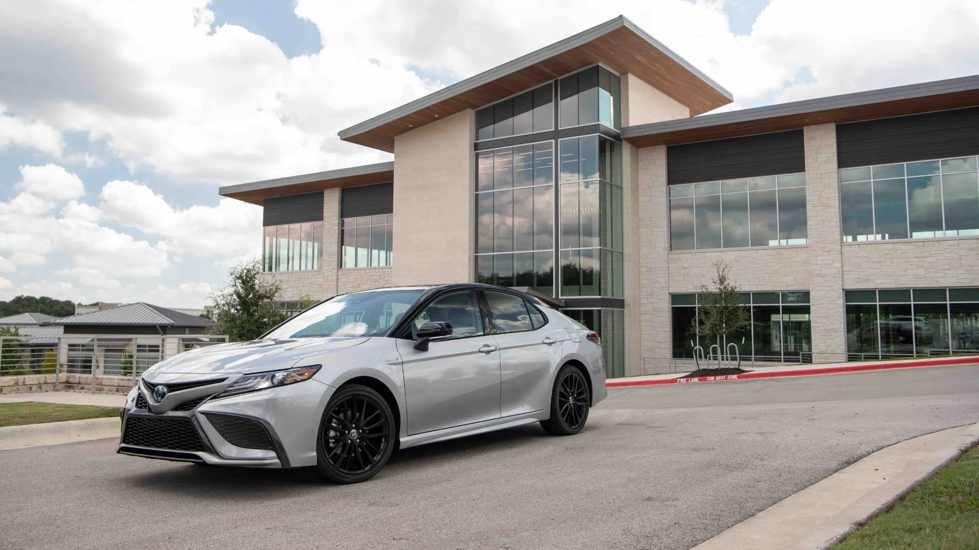 Xe Toyota Camry 2022 Hybrid màu bạc đỗ bên ngoài một tòa nhà hiện đại