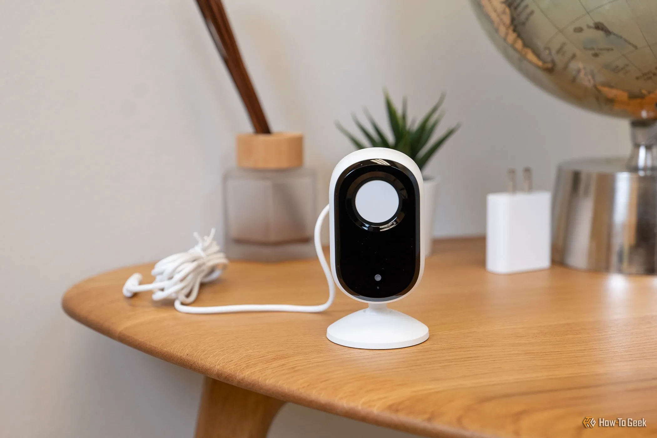 Camera an ninh Arlo Essential Indoor Cam (2K) màu trắng đặt trên bàn, màn che riêng tư đang đóng.